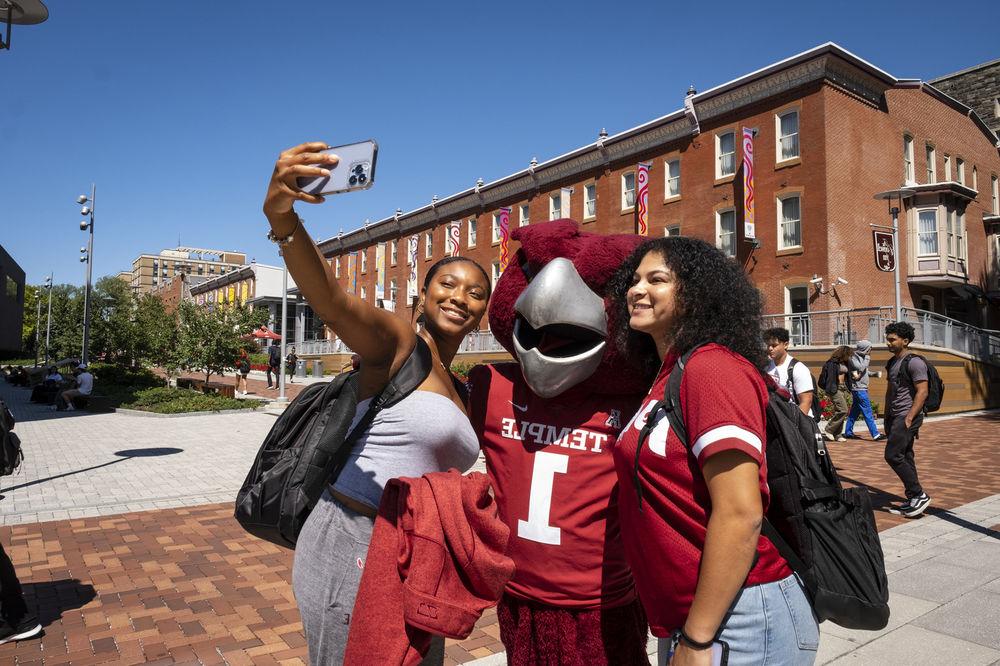 Two Temple students taking a selfie with Hooter, Temple's Owl mascot. 